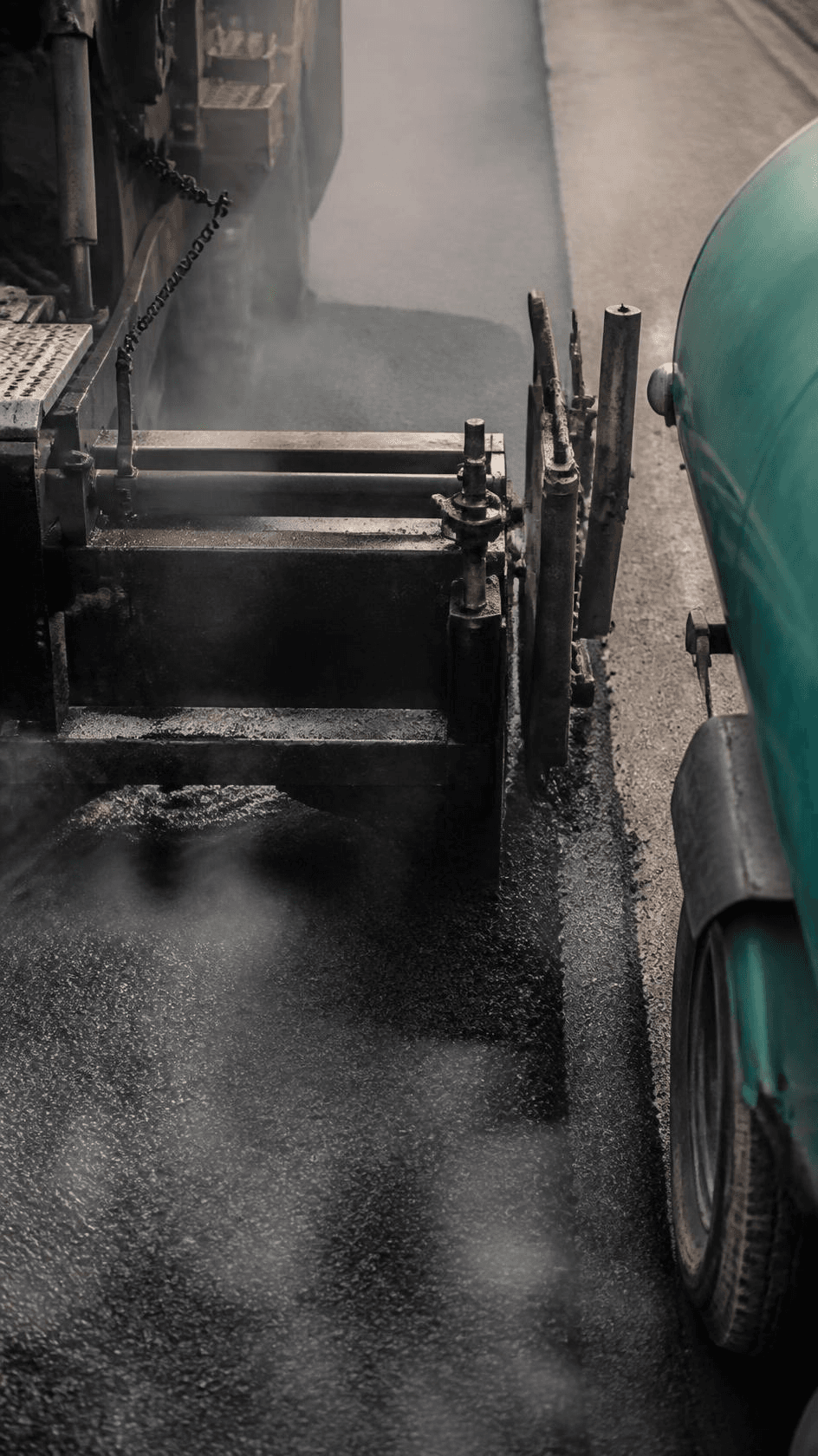 The screed edge of a paver spreading fresh asphalt.