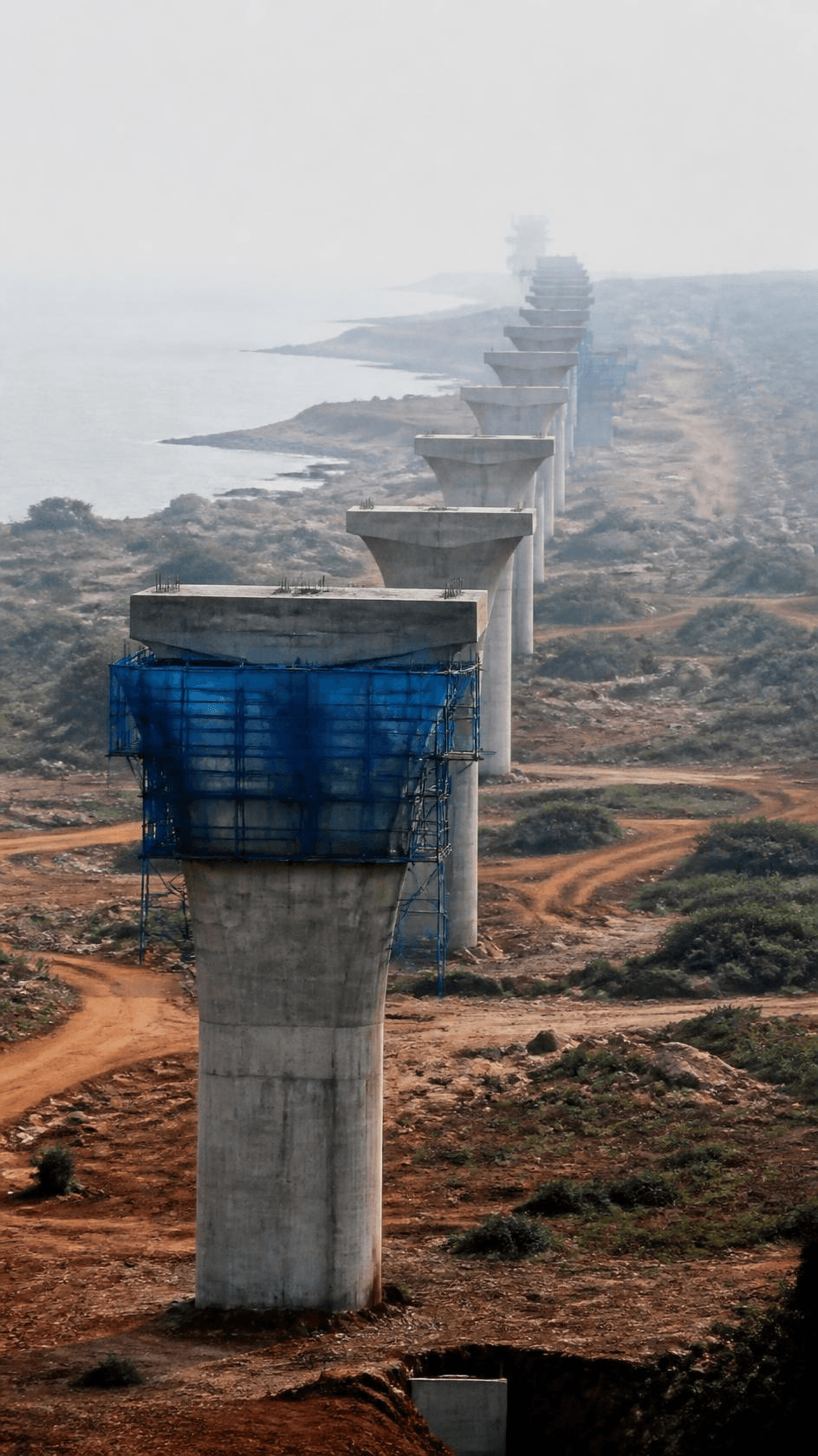 A line of completed bridge piers marching into coastal haze.