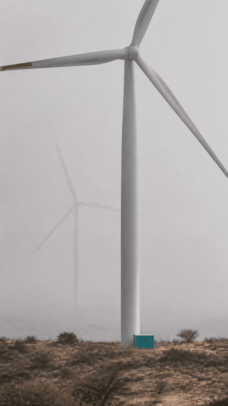 A wind turbine tower rising out of morning haze on dry plateau ground.