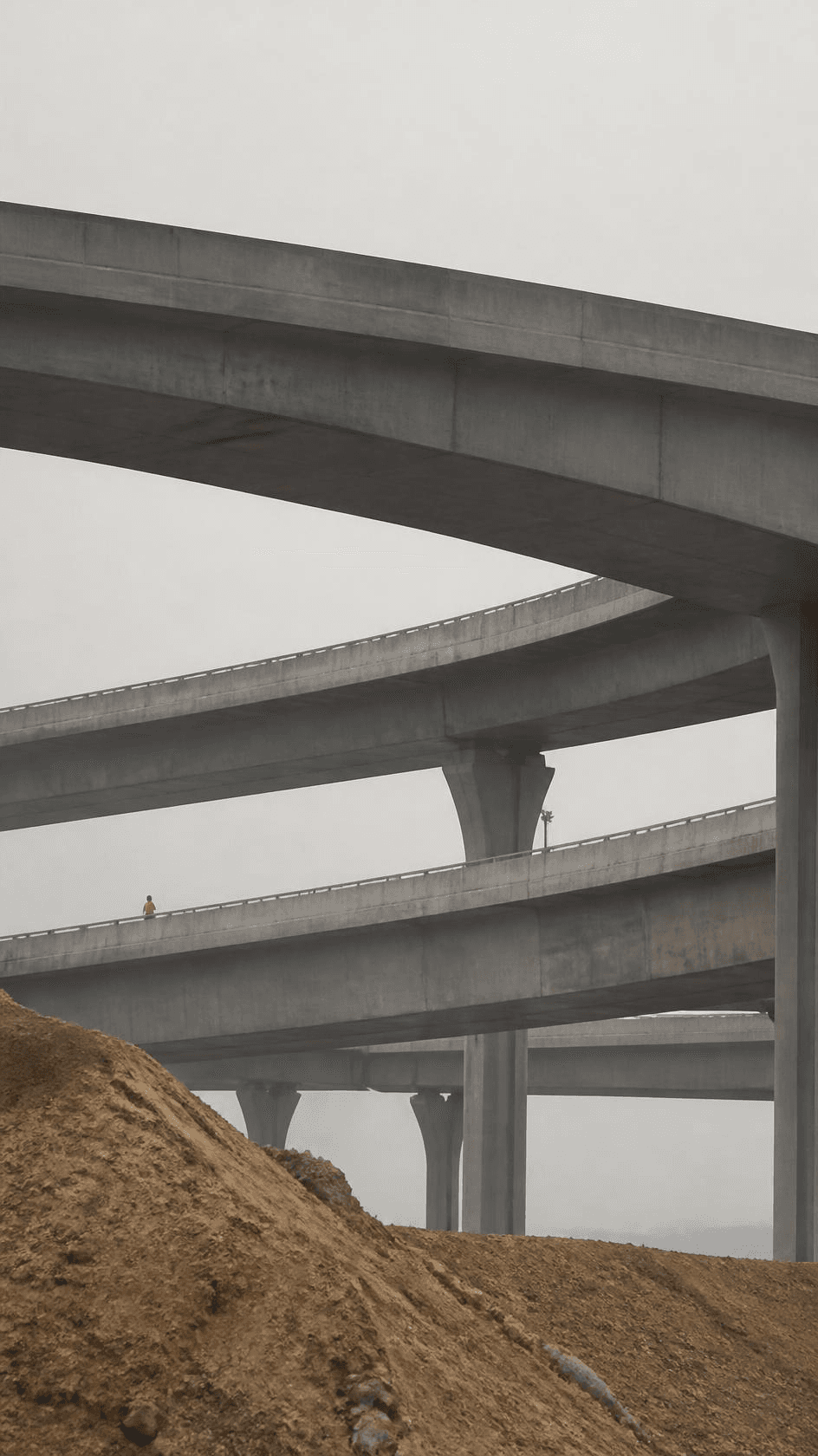 Stacked concrete interchange ramps curving above bare earth.
