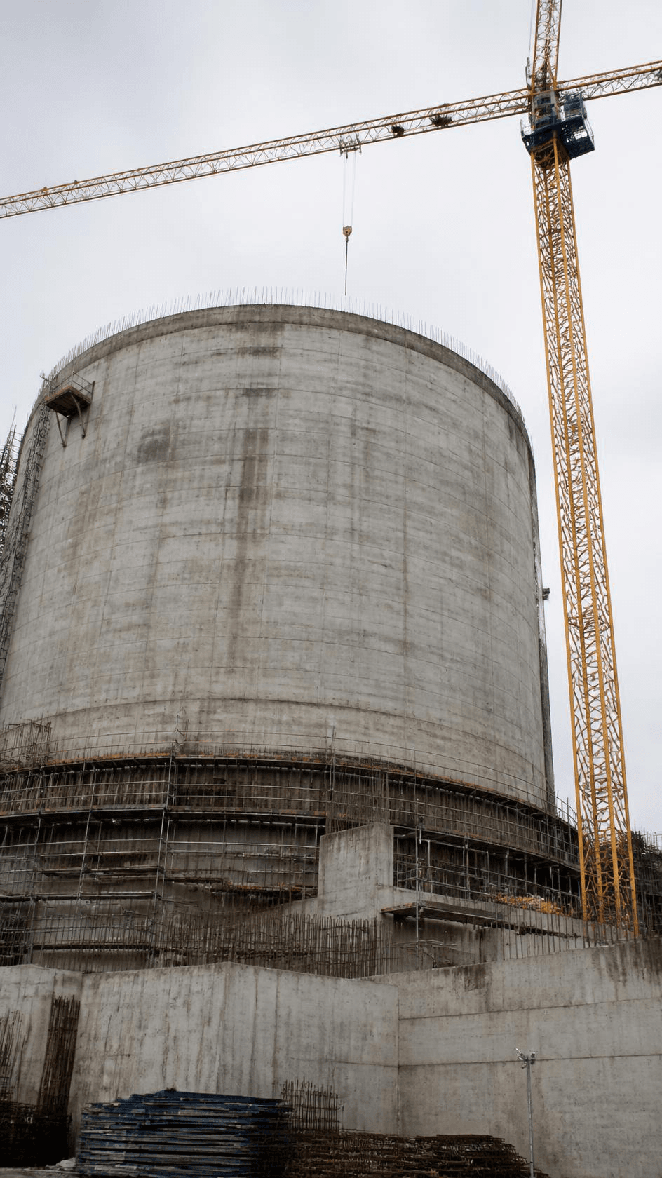 A cylindrical concrete containment structure under construction with a tower crane alongside.