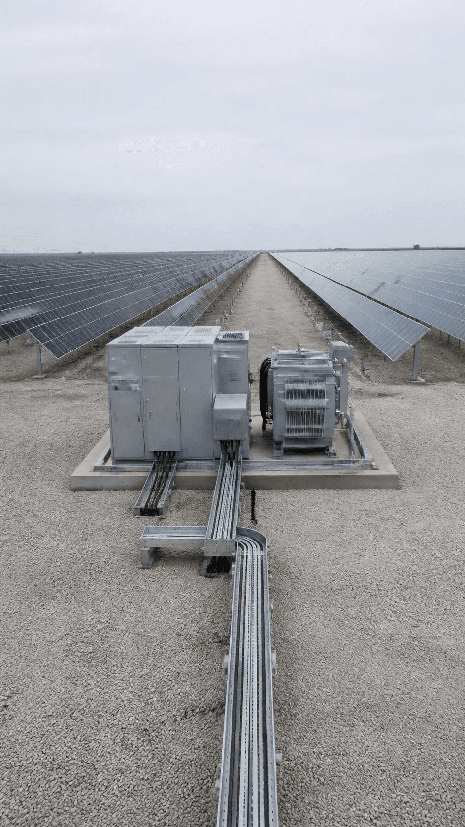 An inverter and transformer skid on gravel between rows of solar panels.