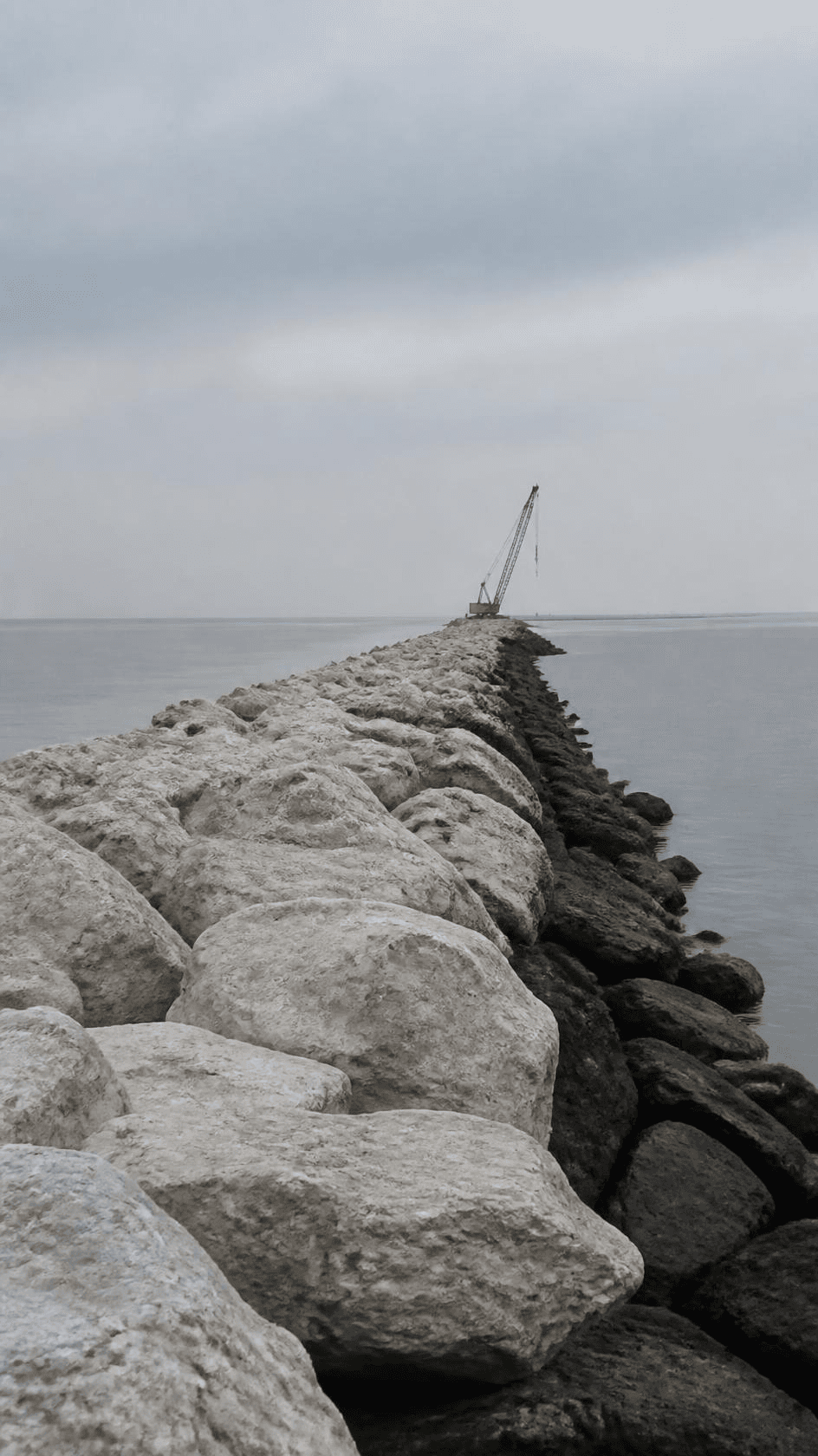 Rock armour placed along a breakwater receding into flat grey water.