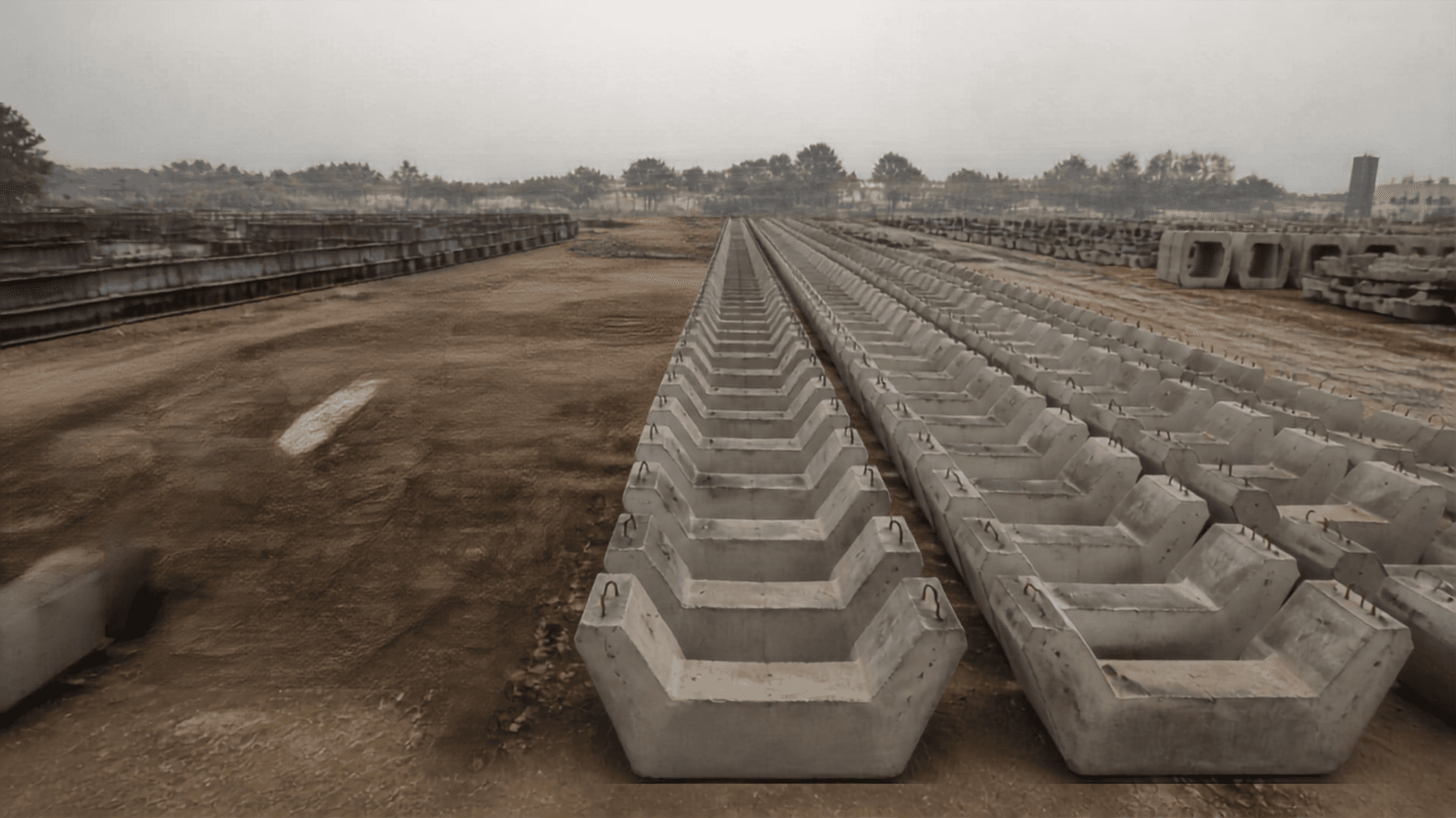 Rows of identical U-shaped precast concrete metro girder segments stored on open ground, receding in strict lines into haze.