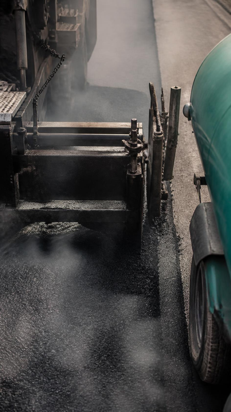 The screed edge of a paver spreading fresh asphalt.