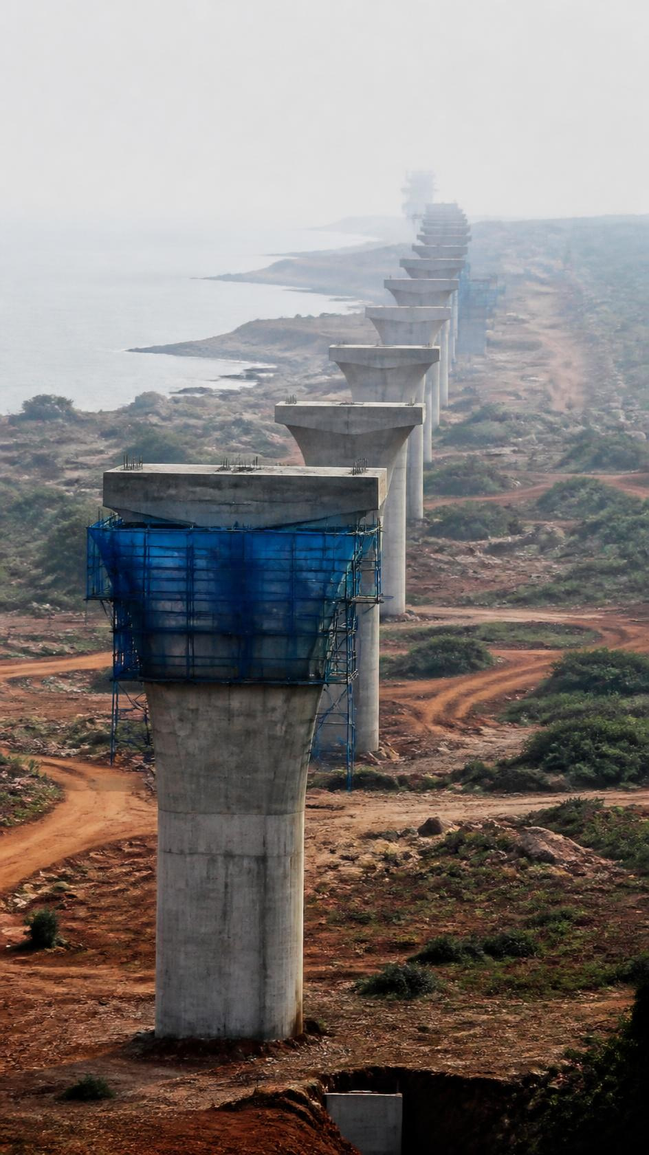 A line of completed bridge piers marching into coastal haze.