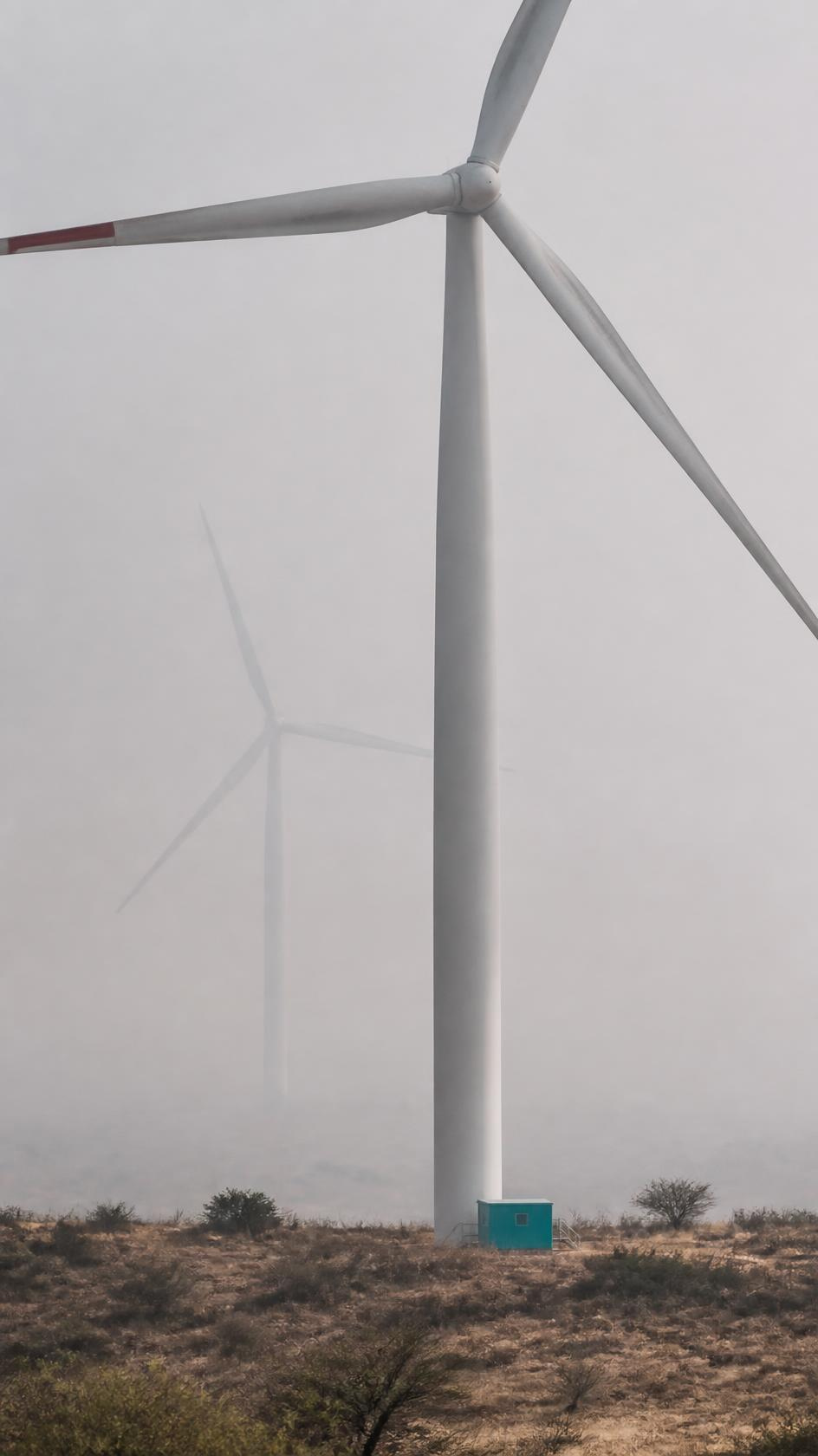 A wind turbine tower rising out of morning haze on dry plateau ground.
