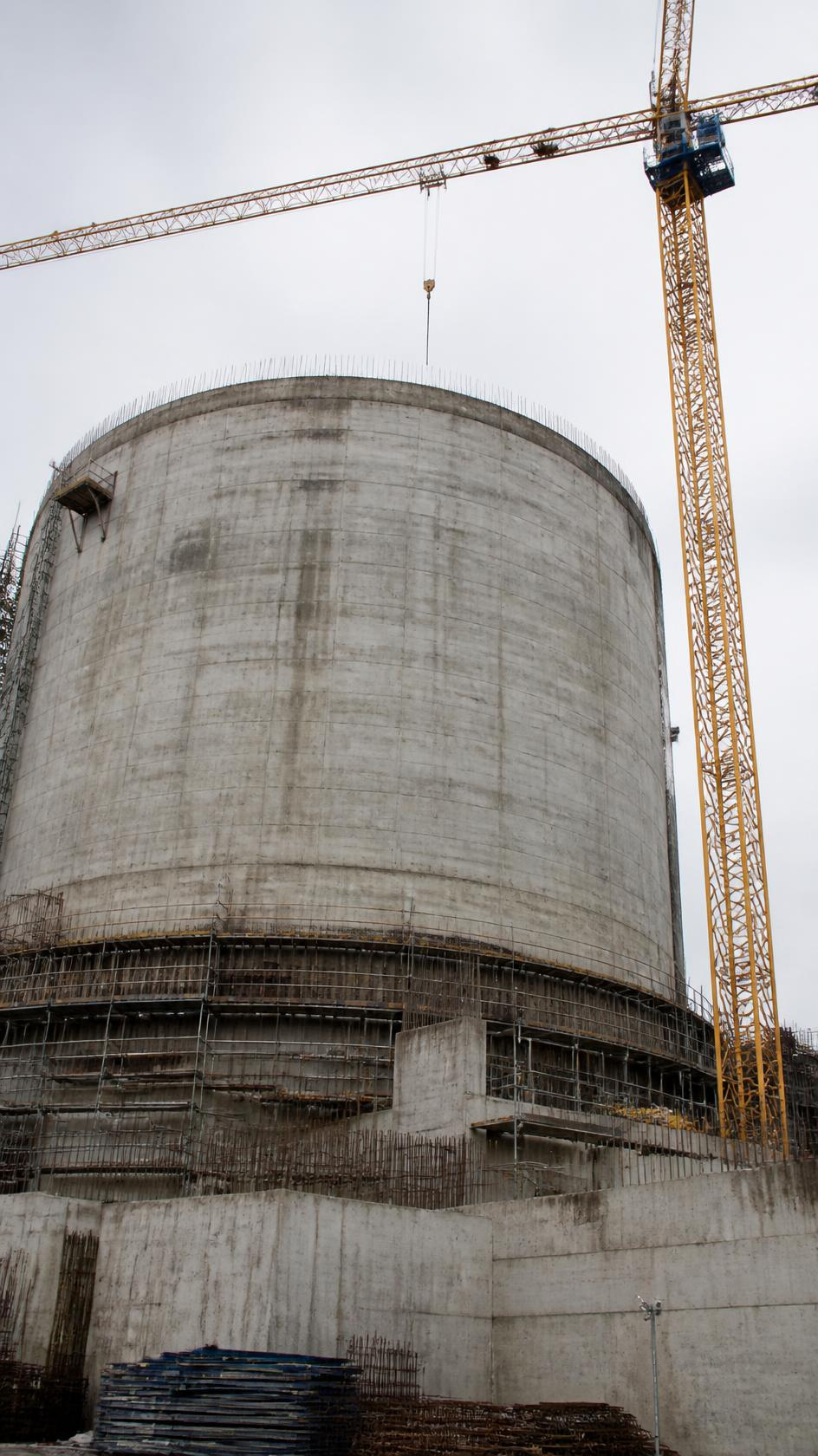 A cylindrical concrete containment structure under construction with a tower crane alongside.