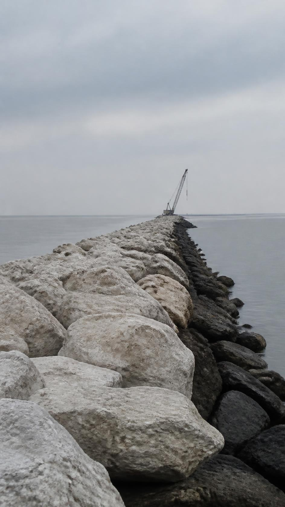 Rock armour placed along a breakwater receding into flat grey water.