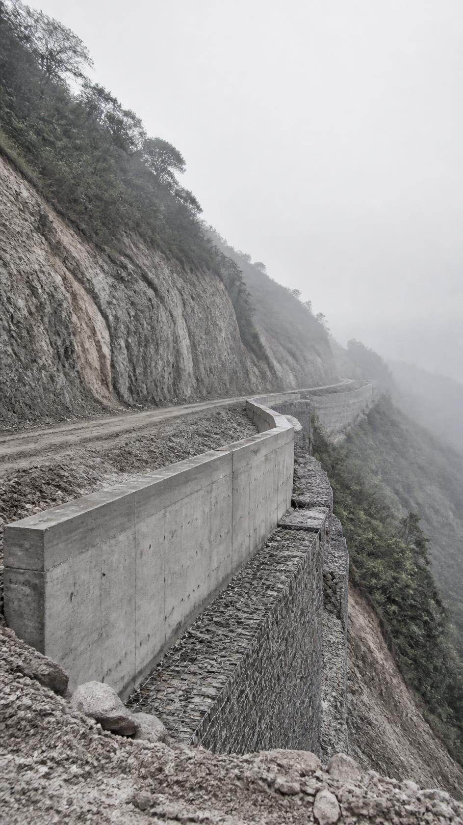 New road formation cut into a steep forested hillside with retaining wall